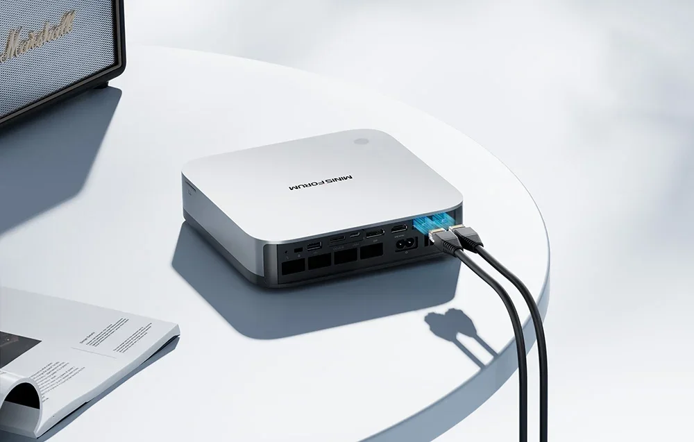 Baltas mini kompiuteris iš galo su prijungtais tinklo kabeliais, USB ir HDMI jungtimis