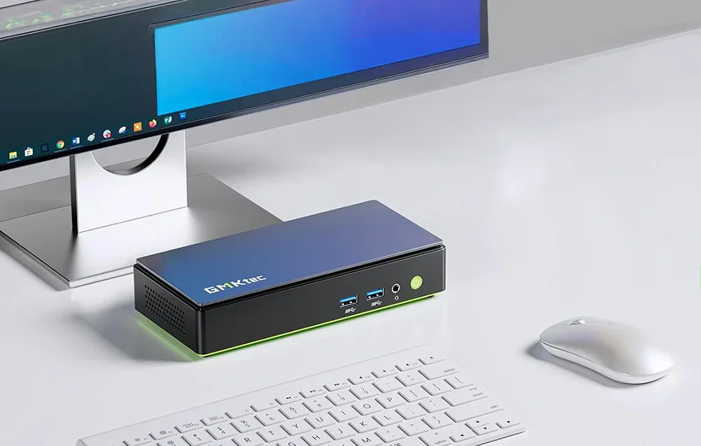 GMKtec K13 Mini PC stovi ant stalo šalia monitoriaus, klaviatūros ir pelės modernioje minimalistinėje darbo vietoje.